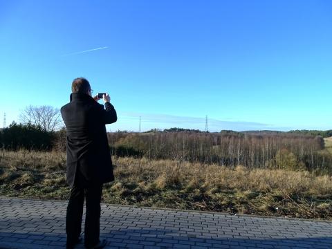 Zdjęcie: Adam Bodnar stoi t tyłem z aparatem, na horyzoncie linia przesyłowa