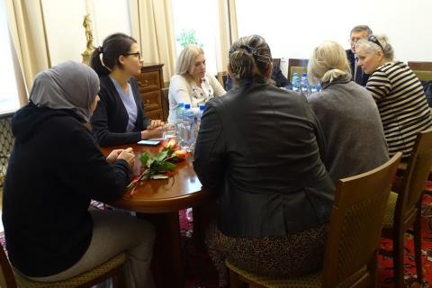 zdjęcie: przy stole siedzi kilka osób, przed jedną z kobiet leżą róże