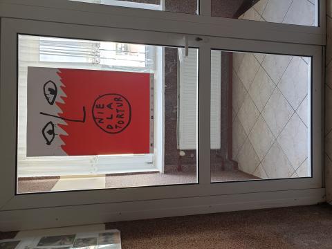 Na zdjęciu widać przeszklone drzwi, na których naklejono plakat przedstawiający biało-czerwoną twarz z napisem: nie dla tortur