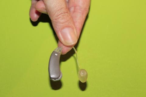 Ręka trzymająca małe urządzenie ze słuchaweczką, zielone tło