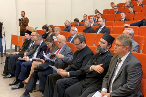 Ludzie na sali audytoryjnej, w tym ksiądz prawosławny