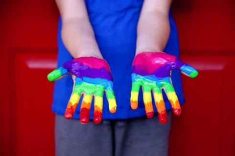 Dłonie bawiącego się dziecka pomalowane farbką w kolorach tęczy
