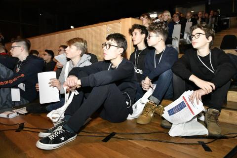 Młodzi ludzie siedzą na schodach auli i słuchają
