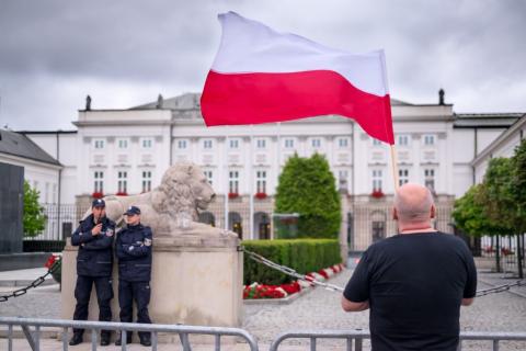 Mężczyzna z biało-czerwoną flagą przed białym budynkiem