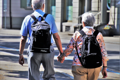 Dwoje starszych ludzi z plecakami idzie przez miasto trzymając się za ręce