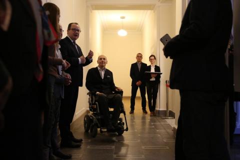 Kilka osób, w tym mężczyzna na wózku, na korytarzu