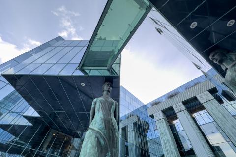 Kolumny, szklana elewacja i detale architektoniczne nowoczesnego budynku, jeden z elementów wspiera się na dużej rzeźbie kobiety w todze