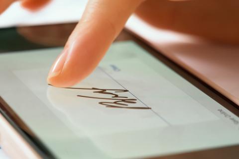 Zbliżenie na tablet, na którym osoba wprowadza palcem podpis własnoręczny